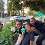 3 kids pose happily with vegetables from the Michigan Avenue branch garden,