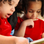 Two African American girls looking at a book, wearing red shirts