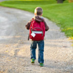 boy wearing red backpack walking on dirt road