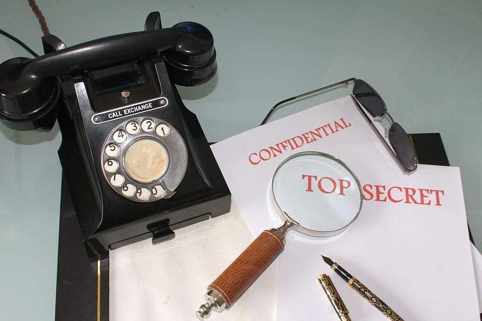 rotary dial phone sitting next to a clipboard that says top secret with a magnifying glass on top