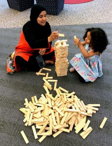 A mom and child stack wooden KEVA planks together.