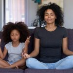 Mom and daughter meditating on a couch.