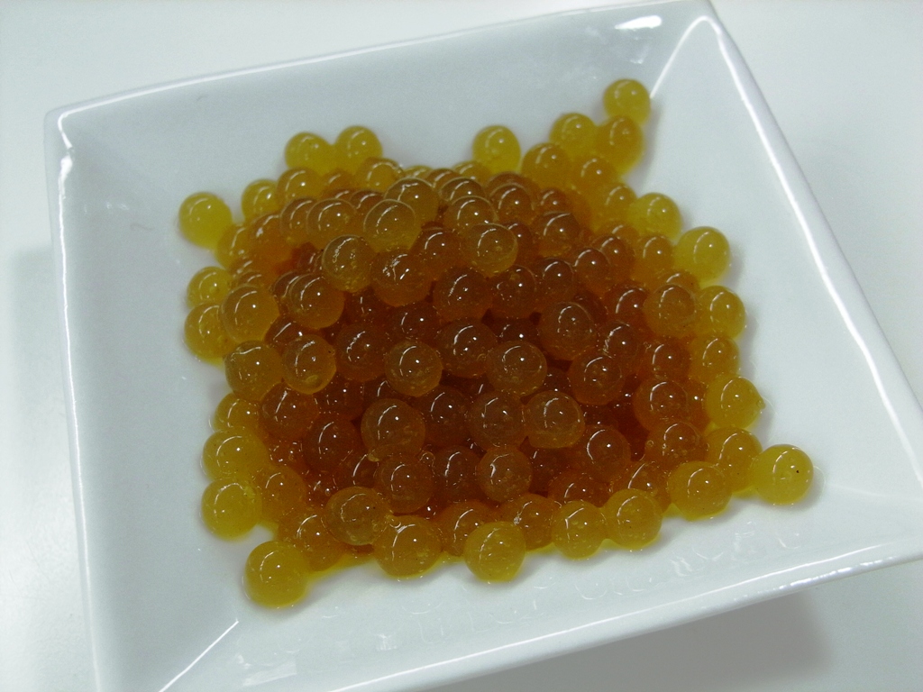 popping boba hundreds or yellow colored popping boba displayed in a white bowl