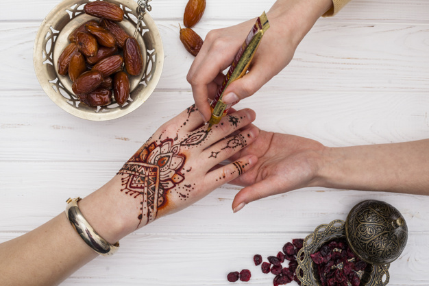 artist-making-mehndi-womans-hand-near-dried-dates-fruit_23-2148074848