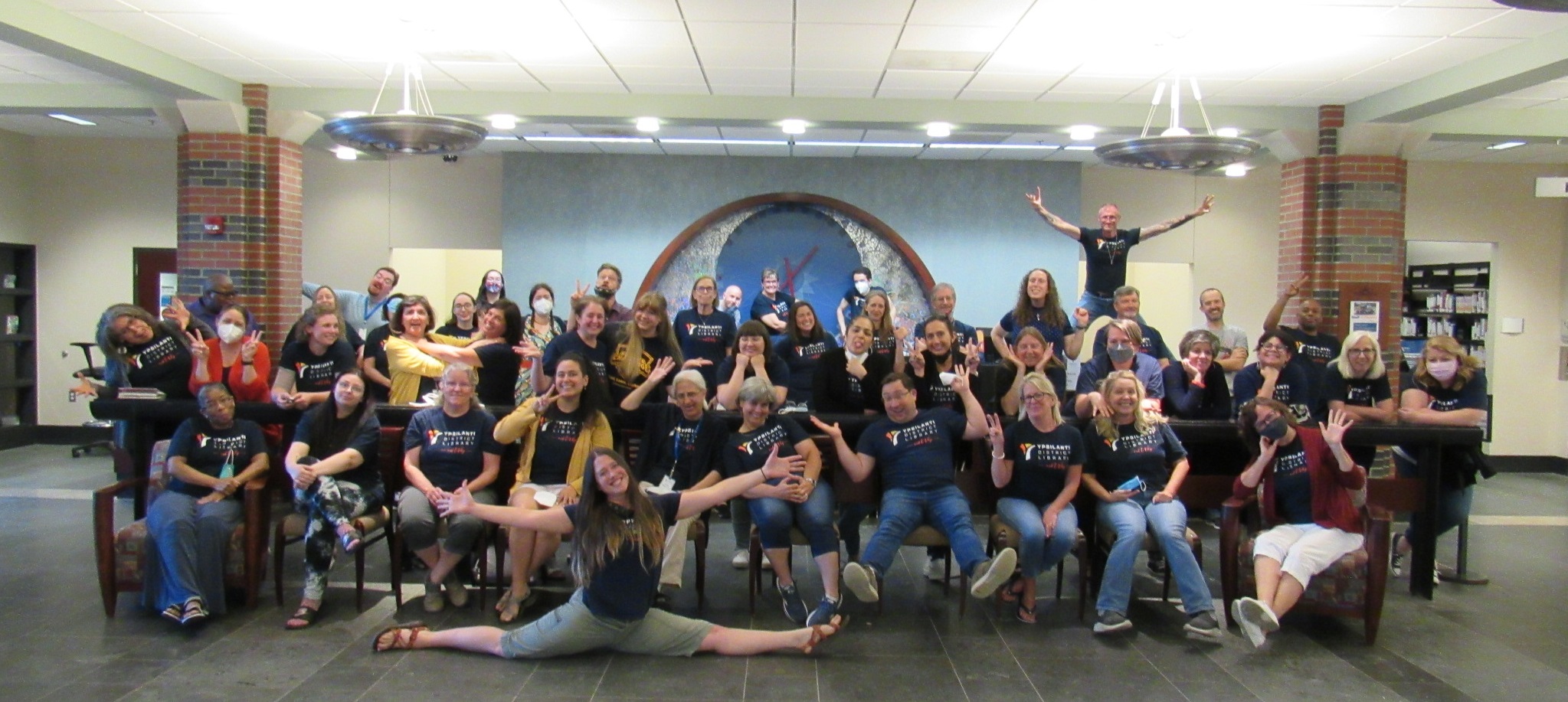 All of the library staff (about 50-60) making various silly poses in front of the front desk at YDL-Whittaker.