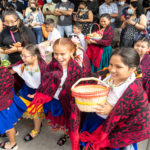 Many young Latinas wear traditional dresses and shawls while carrying baskets.