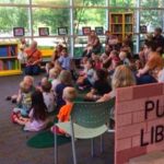 Image of an adult volunteer reading to a group of children in the library