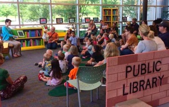 Image of an adult volunteer reading to a group of children in the library