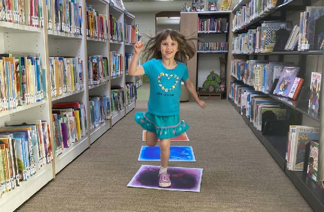 Girl in green shirt jumps on floor tiles with purple, blue, and orange liquids.